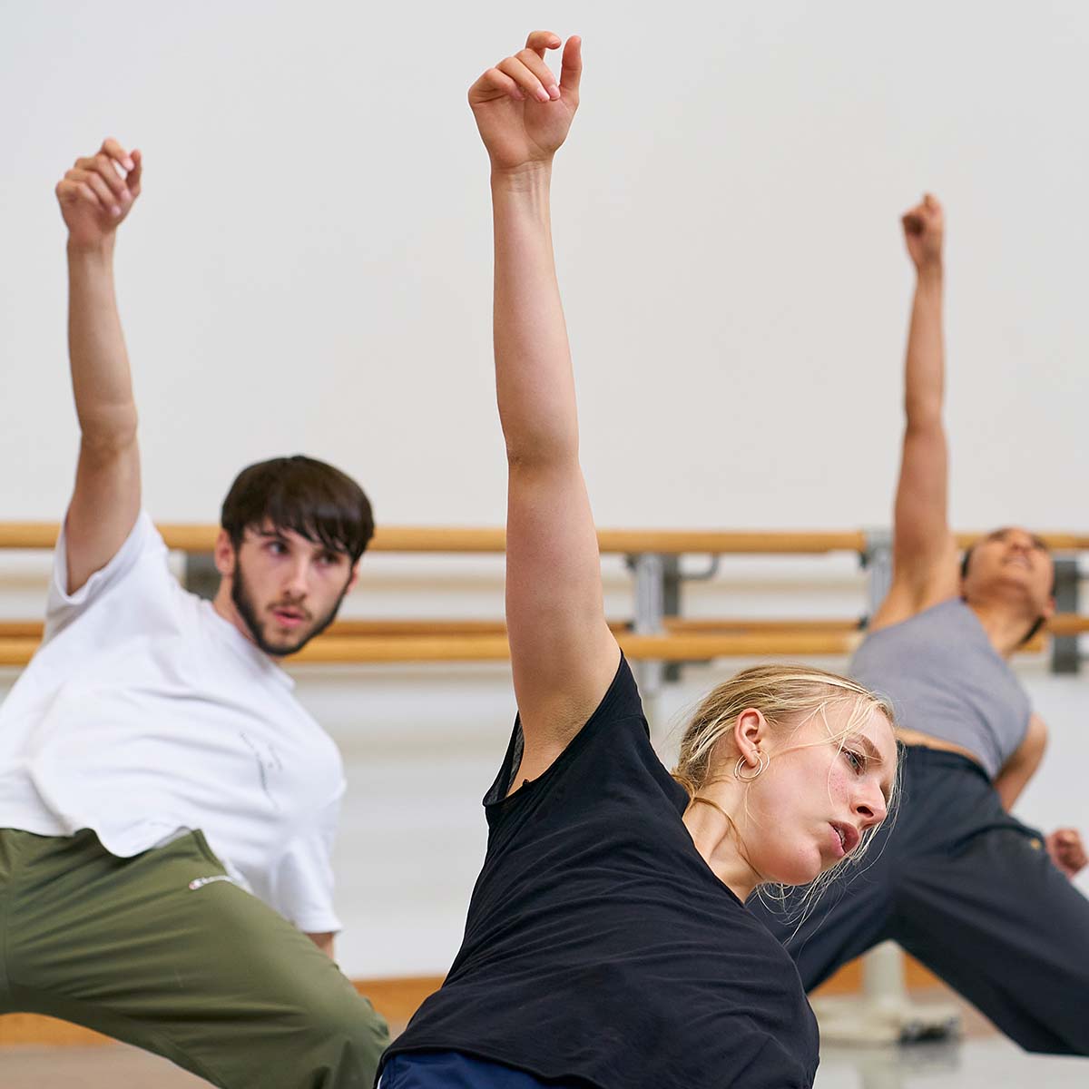 3 dancers in class lean back, reaching up 