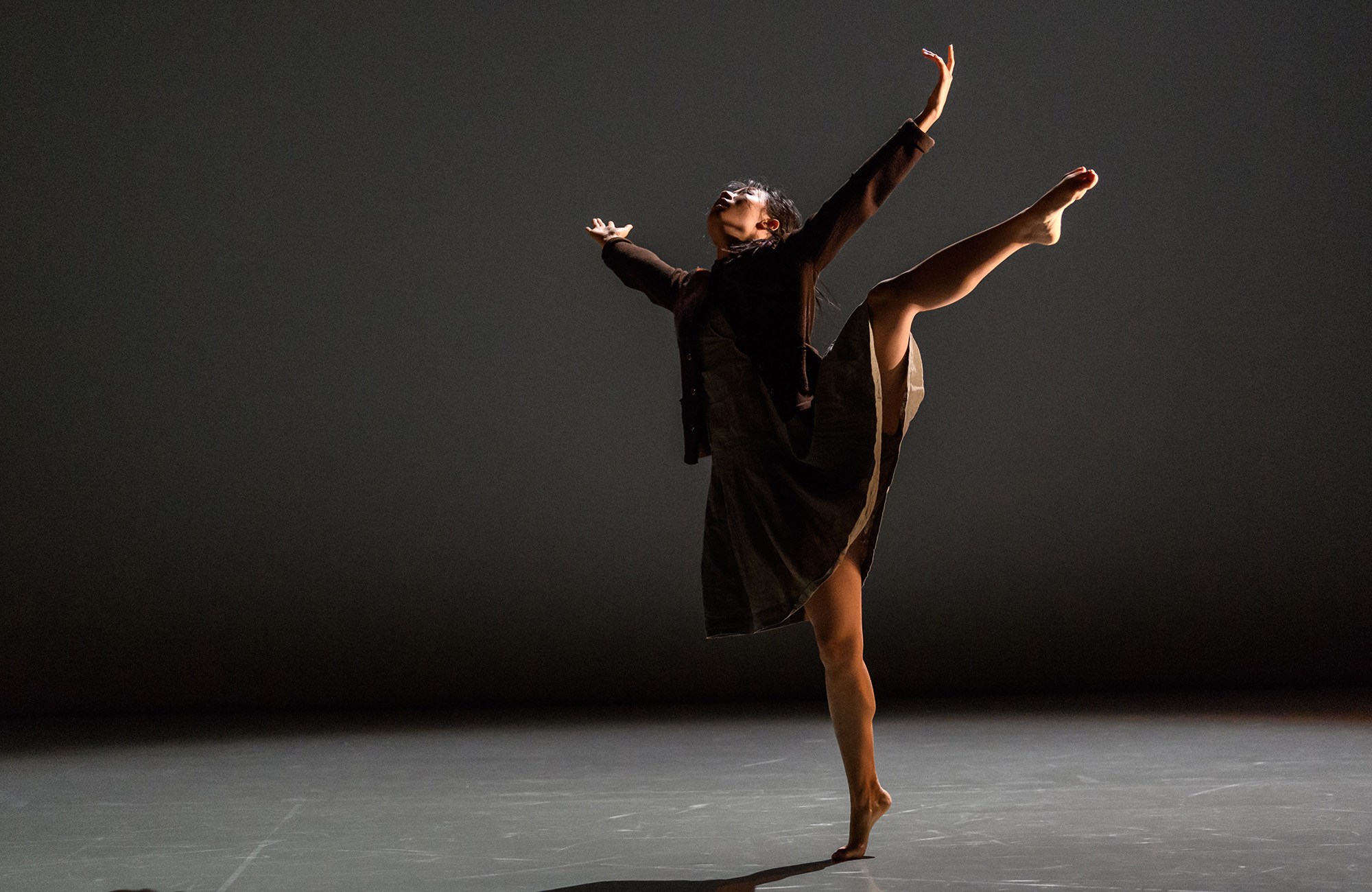 Dancer on releve reaches up with arms open and one leg raised 